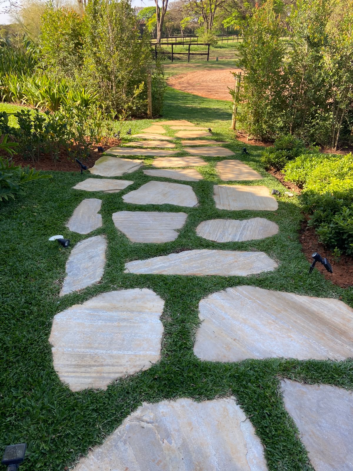 caminho de pedras irregulares (pedra são tomé) sobre grama em jardim bem cuidado com arbustos e iluminação emb
