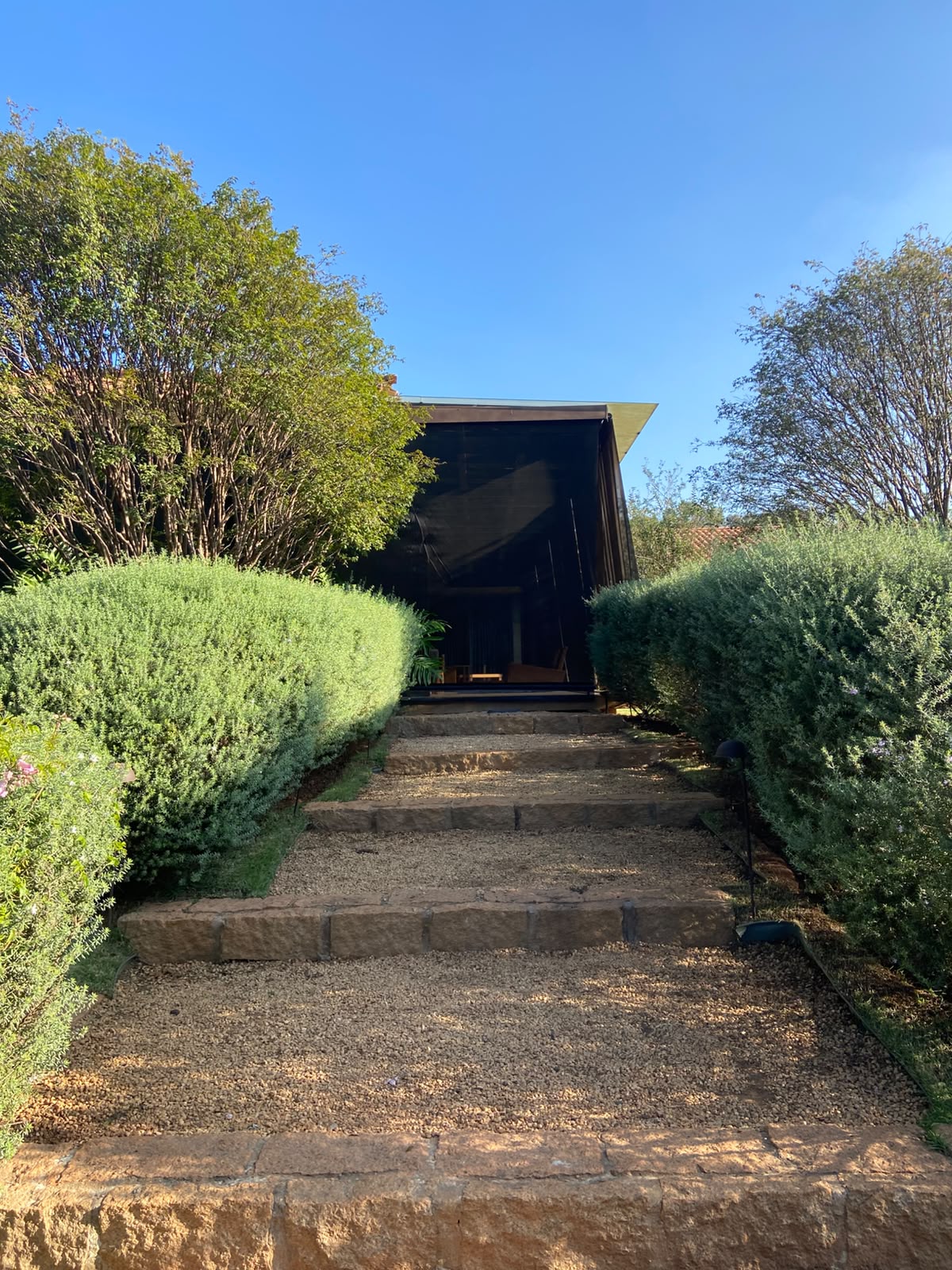 escadaria de pedra com cascalho entre arbustos verdes levando à entrada de uma casa com cobertura escura sob c